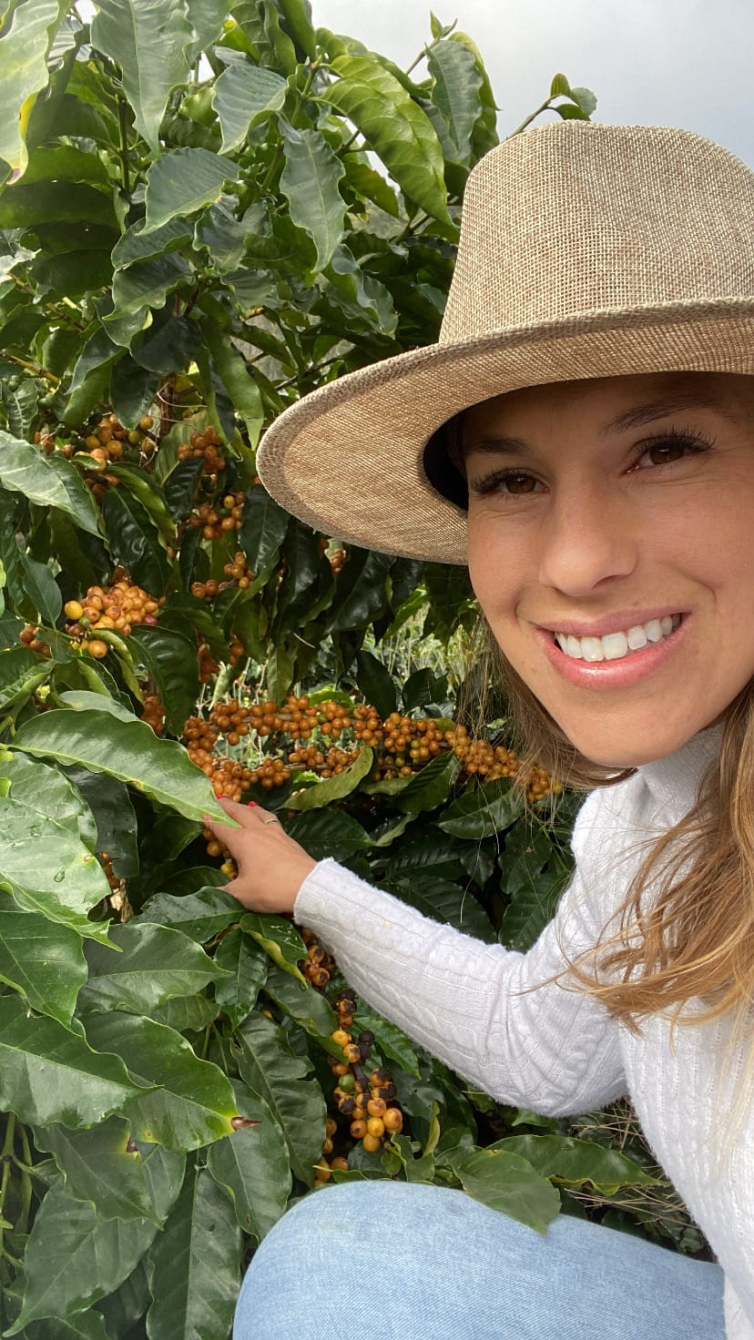 Produtora sorrindo ao lado de frutos amarelos de café